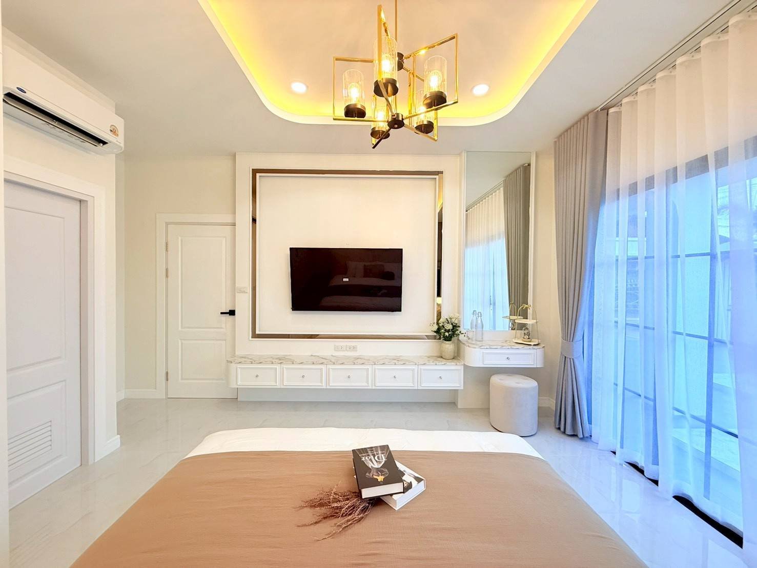 Pattaya_Tropical_2_Village_Dlh535_6 Bright hotel room with wall-mounted TV, marble vanity, and a large mirror framed by warm lighting above a bed side by side with sheer, floor-to-ceiling curtains.