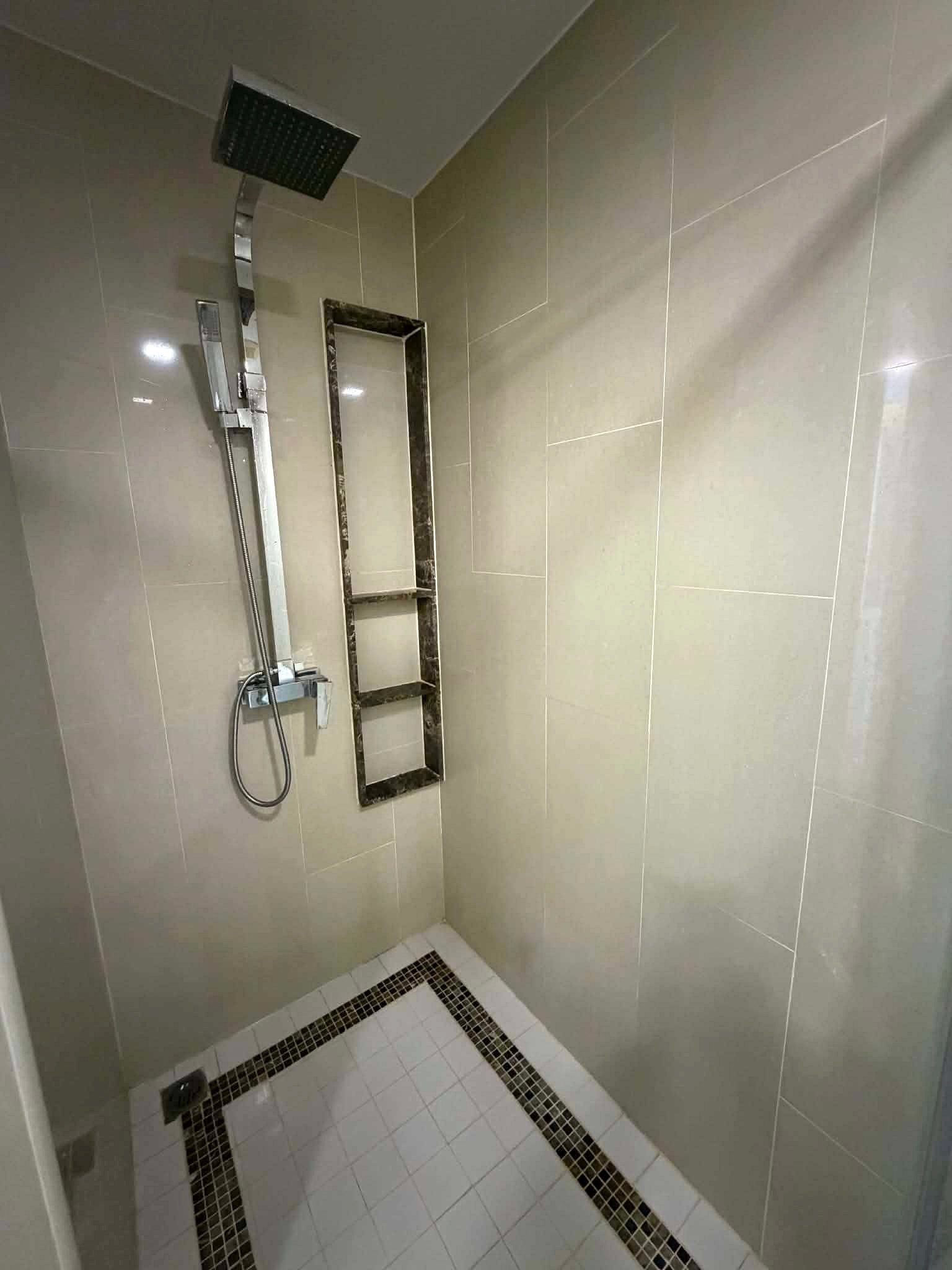 Peak_Tower_Sale_Rent_Dlc365_Rdl337_15 Modern shower area with square rainfall showerhead, handheld wand on a vertical rail, marble-framed square niche, beige tiles, and a white floor with a black mosaic border.