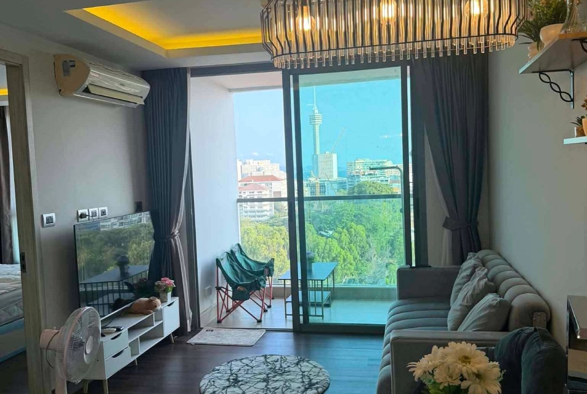 Modern living room with a metal chandelier over sliding balcony doors and a city skyline view, gray sofa and flowers on a white counter in the foreground.