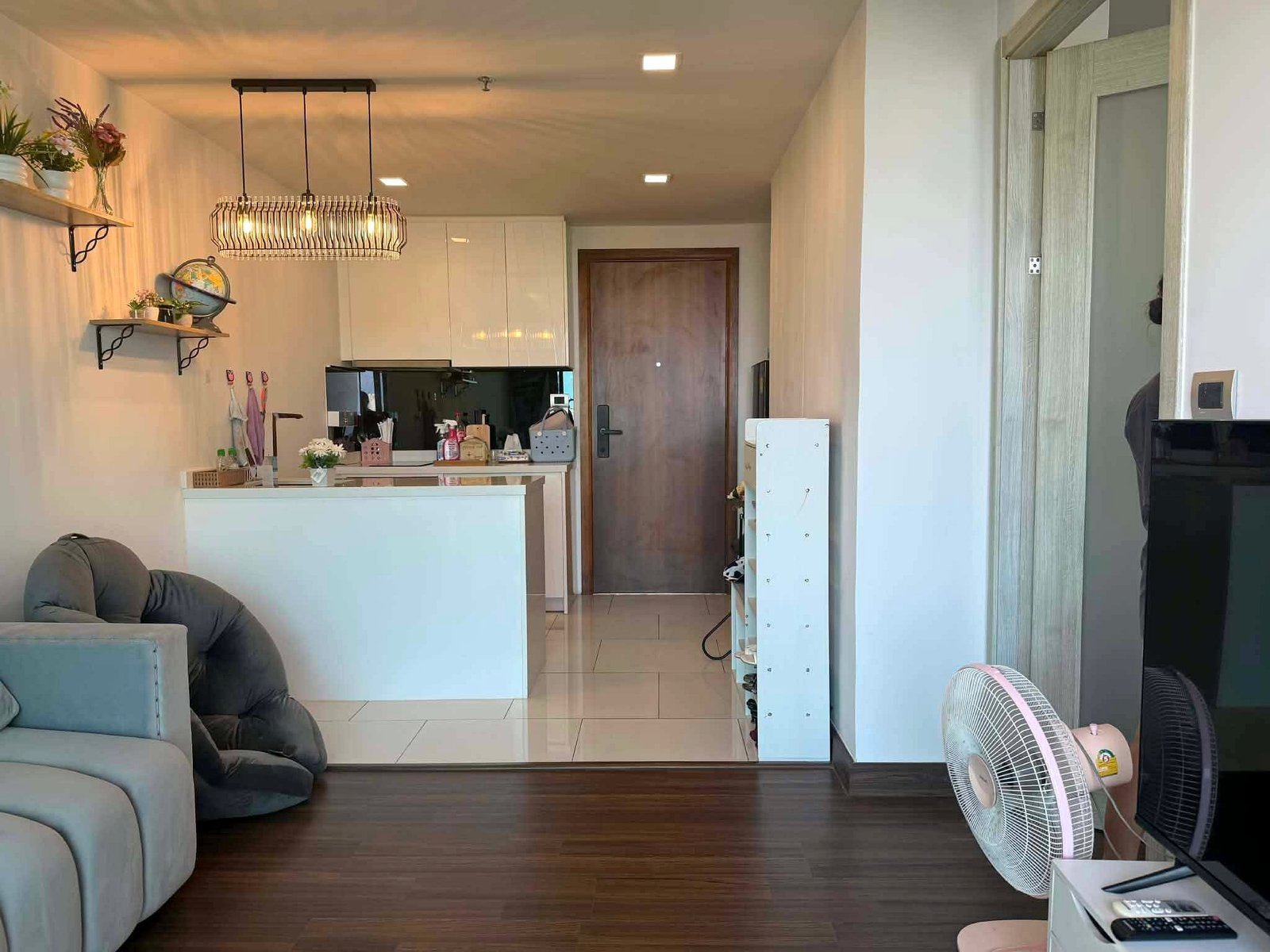 Peak_Tower_Sale_Rent_Dlc365_Rdl337_4 Open-plan living area with dark wood floor, white cabinetry, and a cage-style pendant light hanging over a kitchen island.