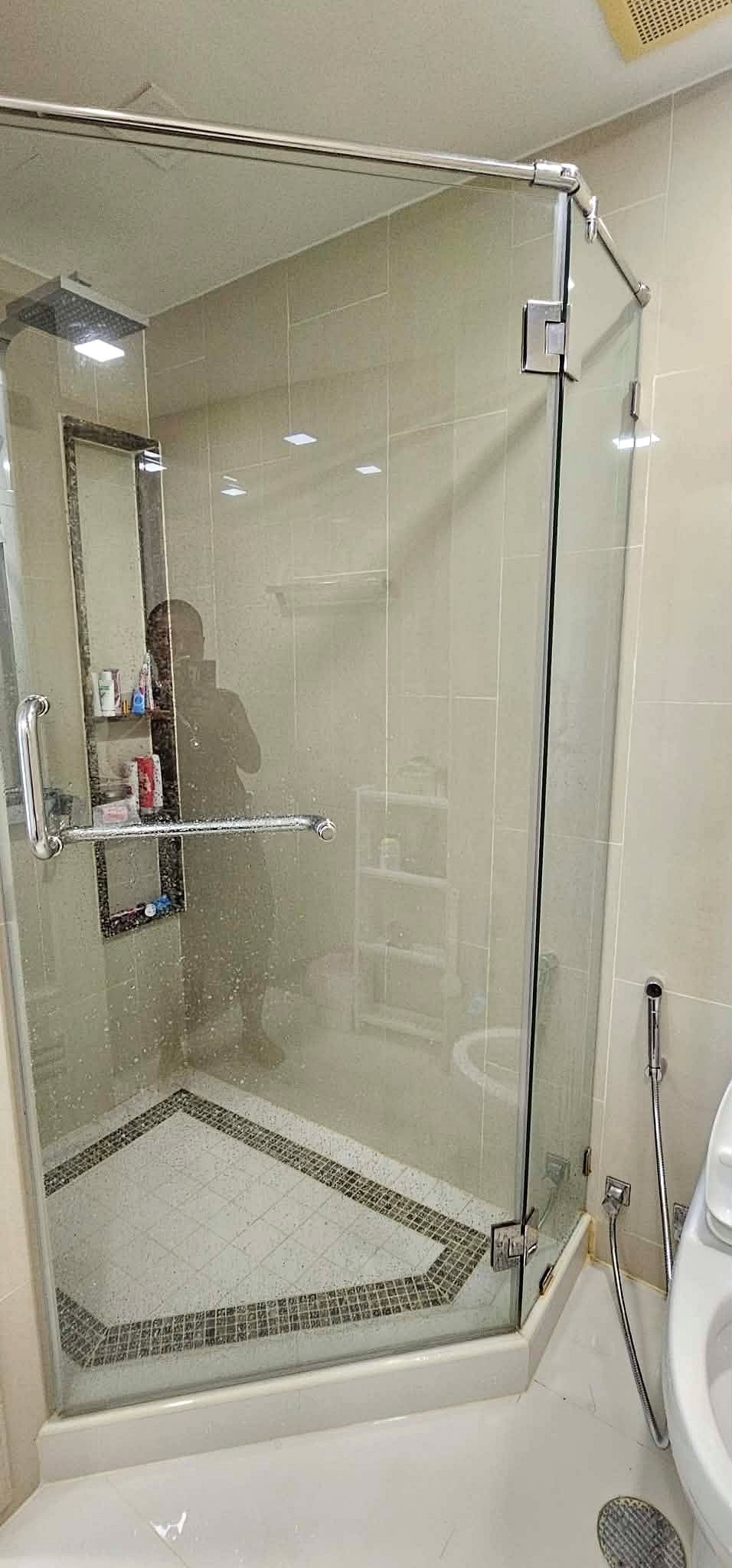 Peak_Tower_Sale_Rent_Dlc365_Rdl337_7 Glass shower enclosure with chrome hardware, tiled walls, and a built-in shelf visible inside; photographer’s silhouette reflected.