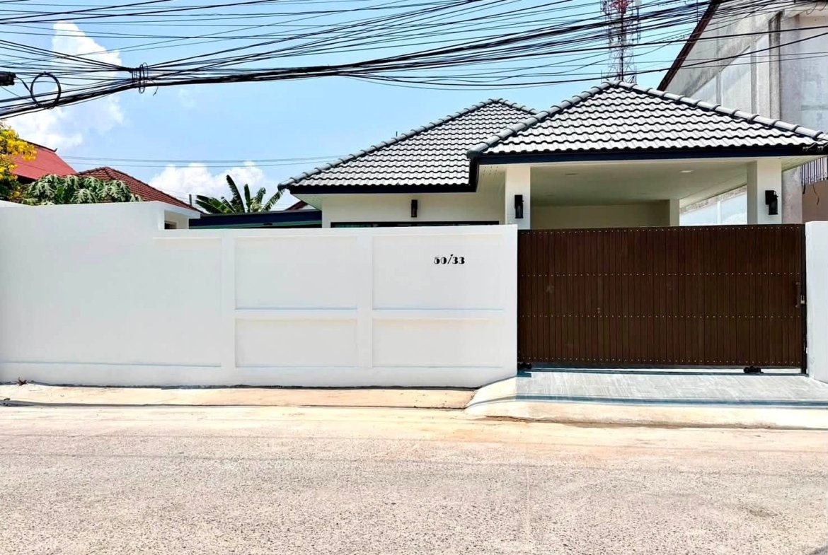 White boundary wall with a dark brown metal gate, house number 50/33, on a sunny street with overhead power lines.