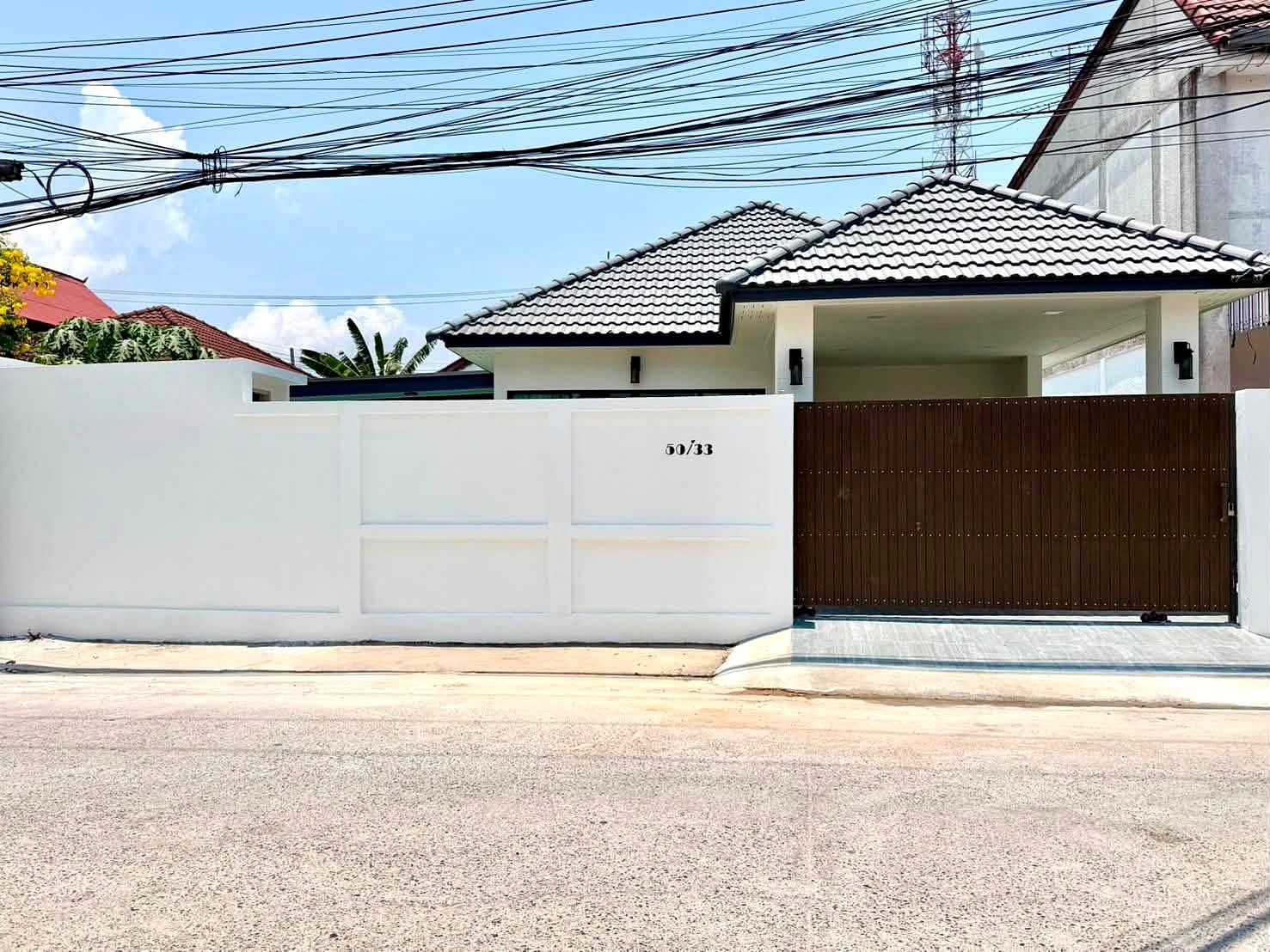 White boundary wall with a dark brown metal gate, house number 50/33, on a sunny street with overhead power lines.