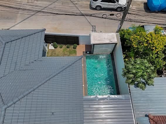 Aerial view of a modern rooftop courtyard with a rectangular pool, gray tiled roofs, a small garden, and a street with power lines beyond.