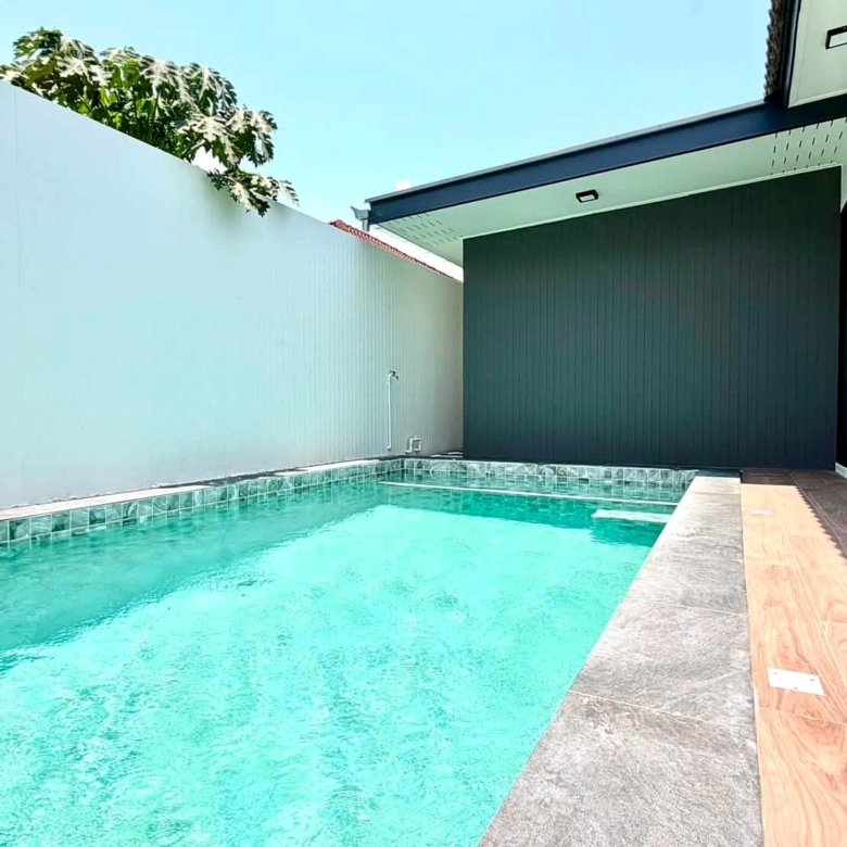 Modern rectangular backyard pool with turquoise water white privacy wall gray coping and a wooden deck beside a dark gray wall and glass doors