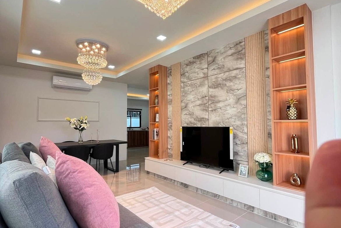 Modern living room with a gray sofa and pink pillows, marble wall panels, TV unit, and open wooden shelves.