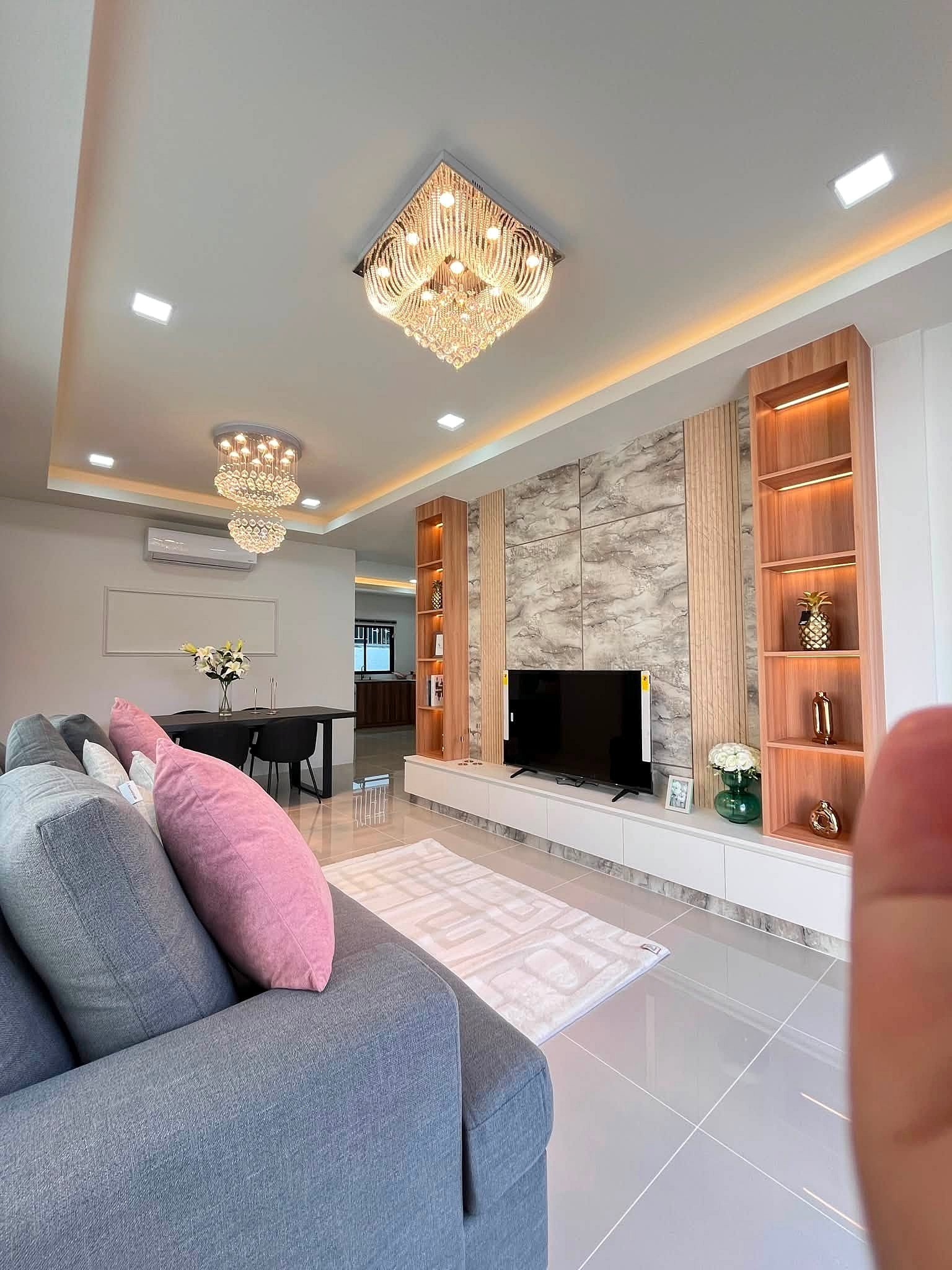 Modern living room with a gray sofa and pink pillows, marble wall panels, TV unit, and open wooden shelves.