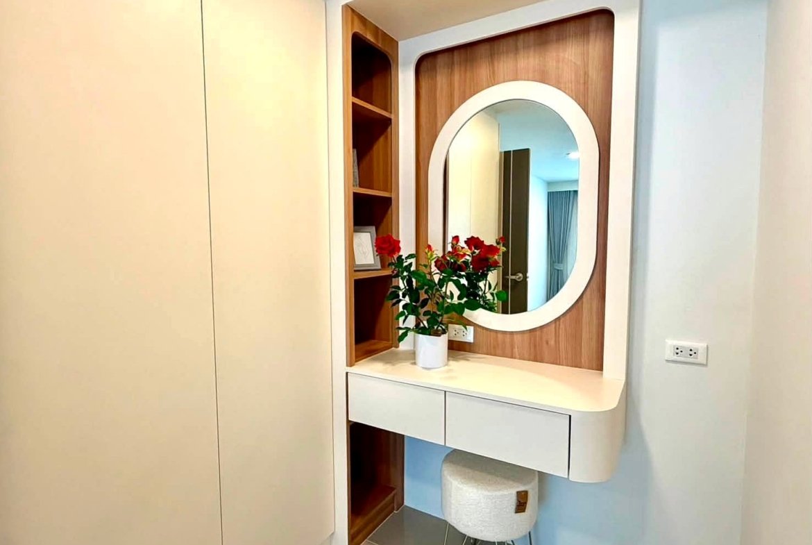 Contemporary vanity with white curved desk, oval mirror, and a vase of red roses on a wood-paneled wall.