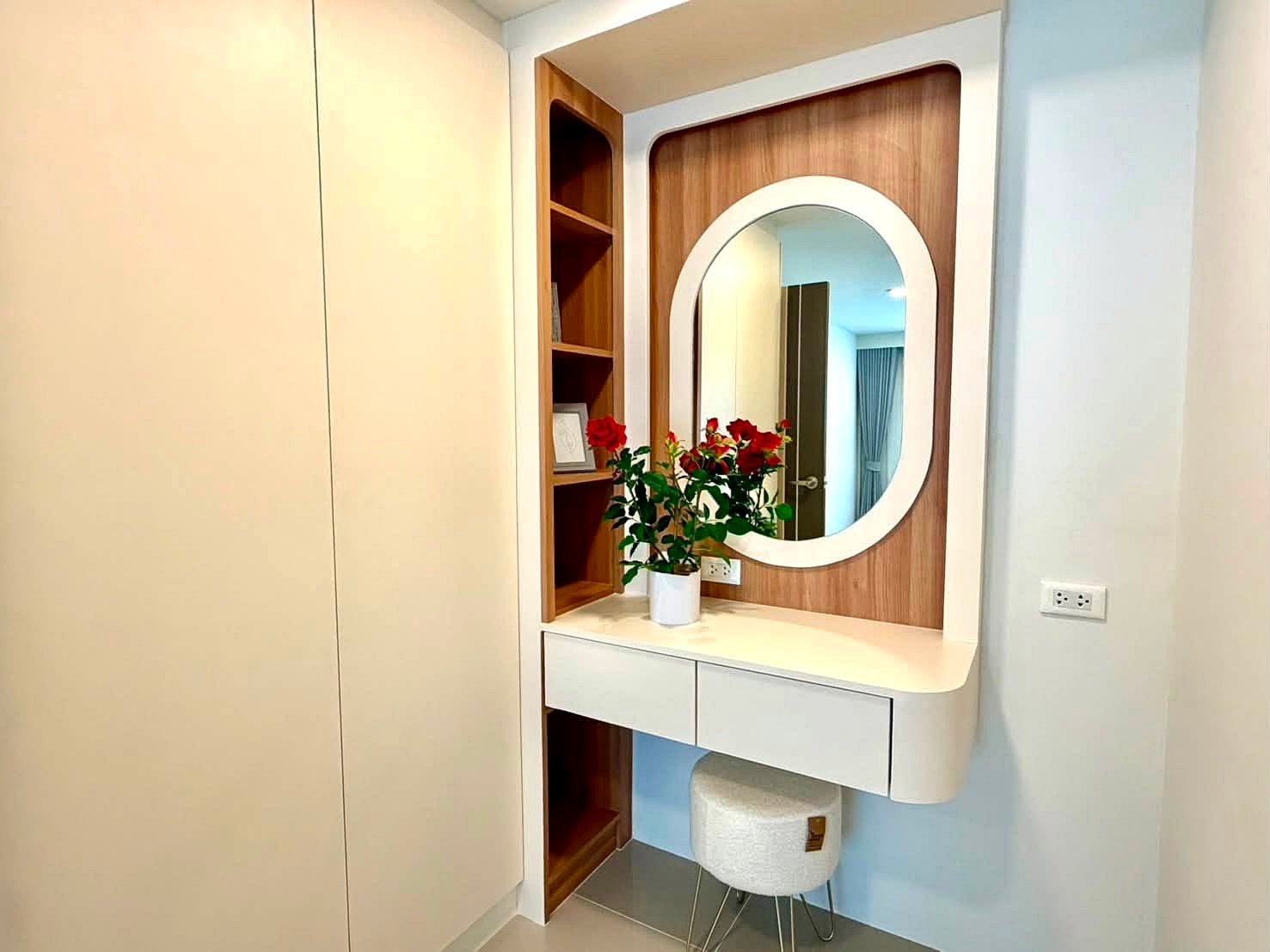 Contemporary vanity with white curved desk, oval mirror, and a vase of red roses on a wood-paneled wall.
