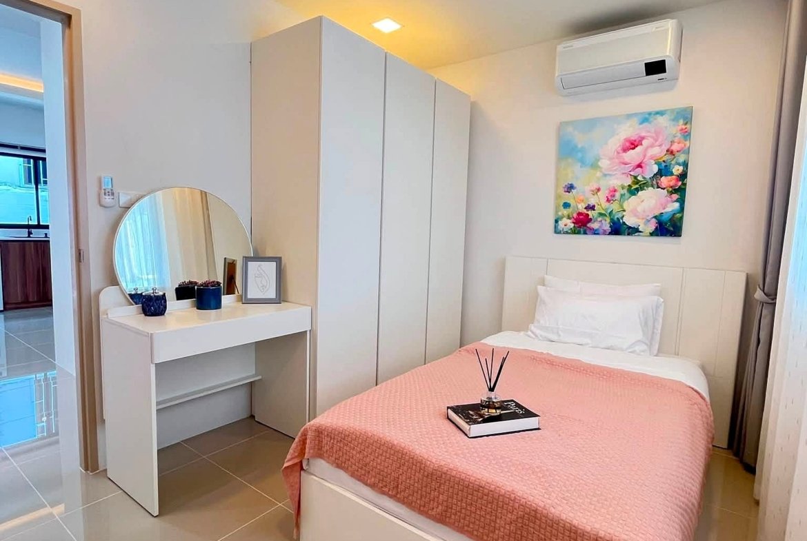 Bright contemporary bedroom with a pink quilt, white bed and built-in wardrobes; a dresser with a round mirror and blue decor accents along the wall art above the bed.