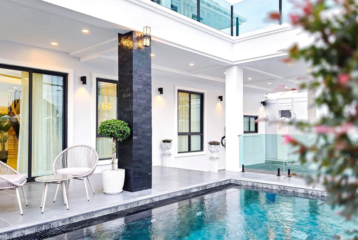 Modern poolside patio with white walls, black stone pillar, glass doors, and outdoor seating by the pool.