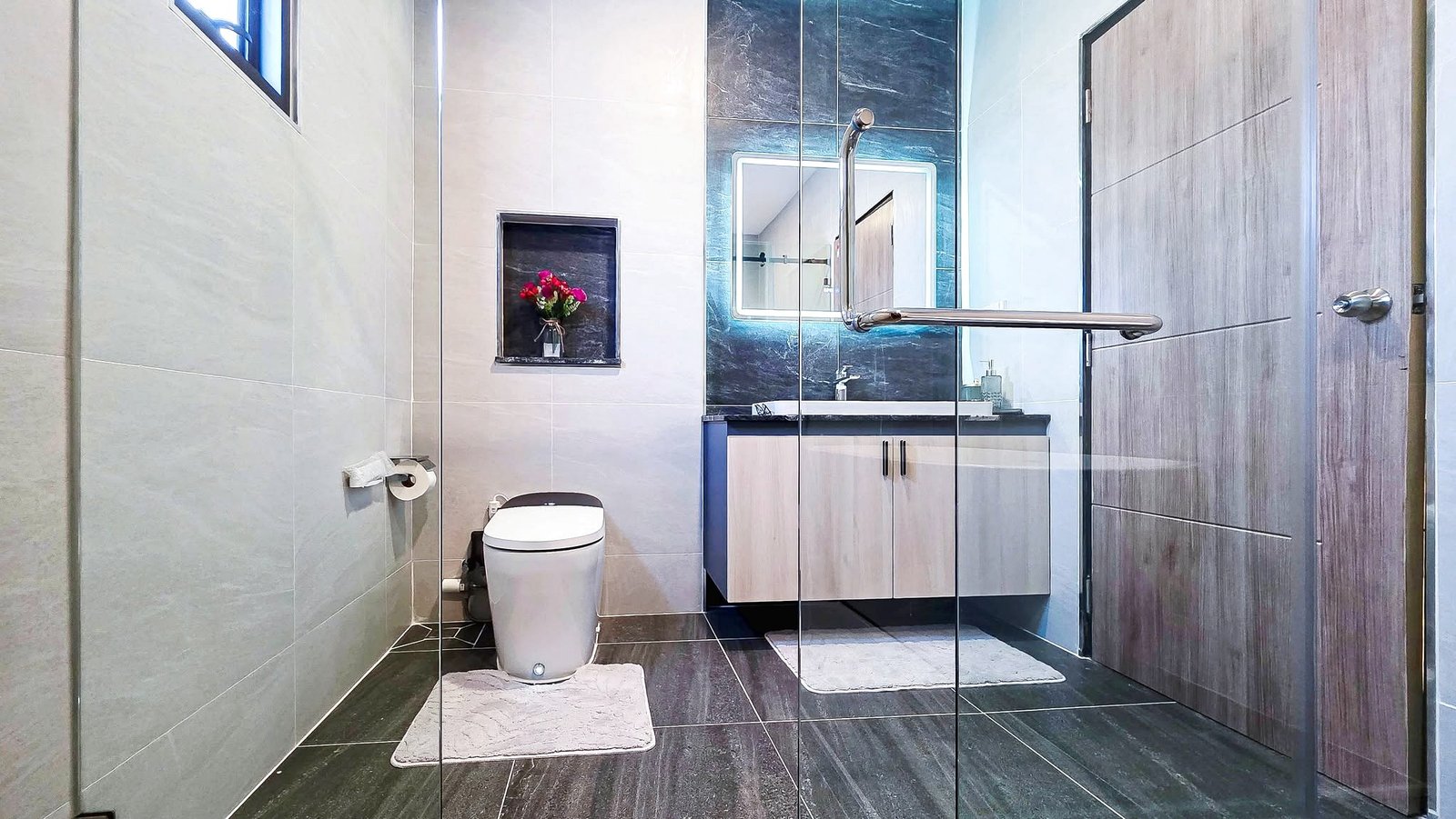 Contemporary bathroom with a glass shower enclosure, toilet, and a vanity; pink flowers in a recessed shelf.