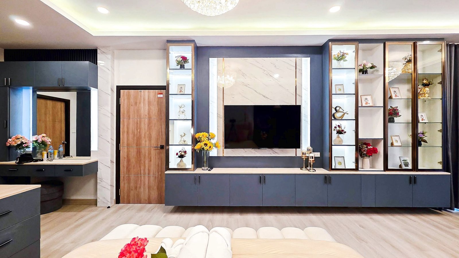 Modern living room built-in unit with a wall-mounted TV, glass display cabinets, and blue-gray cabinetry with marble accents.