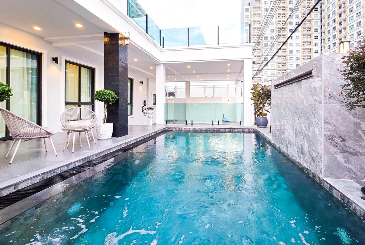 Modern poolside courtyard of a contemporary building with white walls, wicker chairs, and potted trees along a rectangular pool.