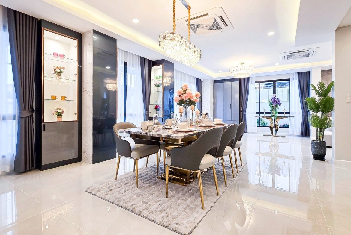 Luxurious dining room with a marble table, gold-legged chairs, crystal chandelier, and large windows with dark curtains.