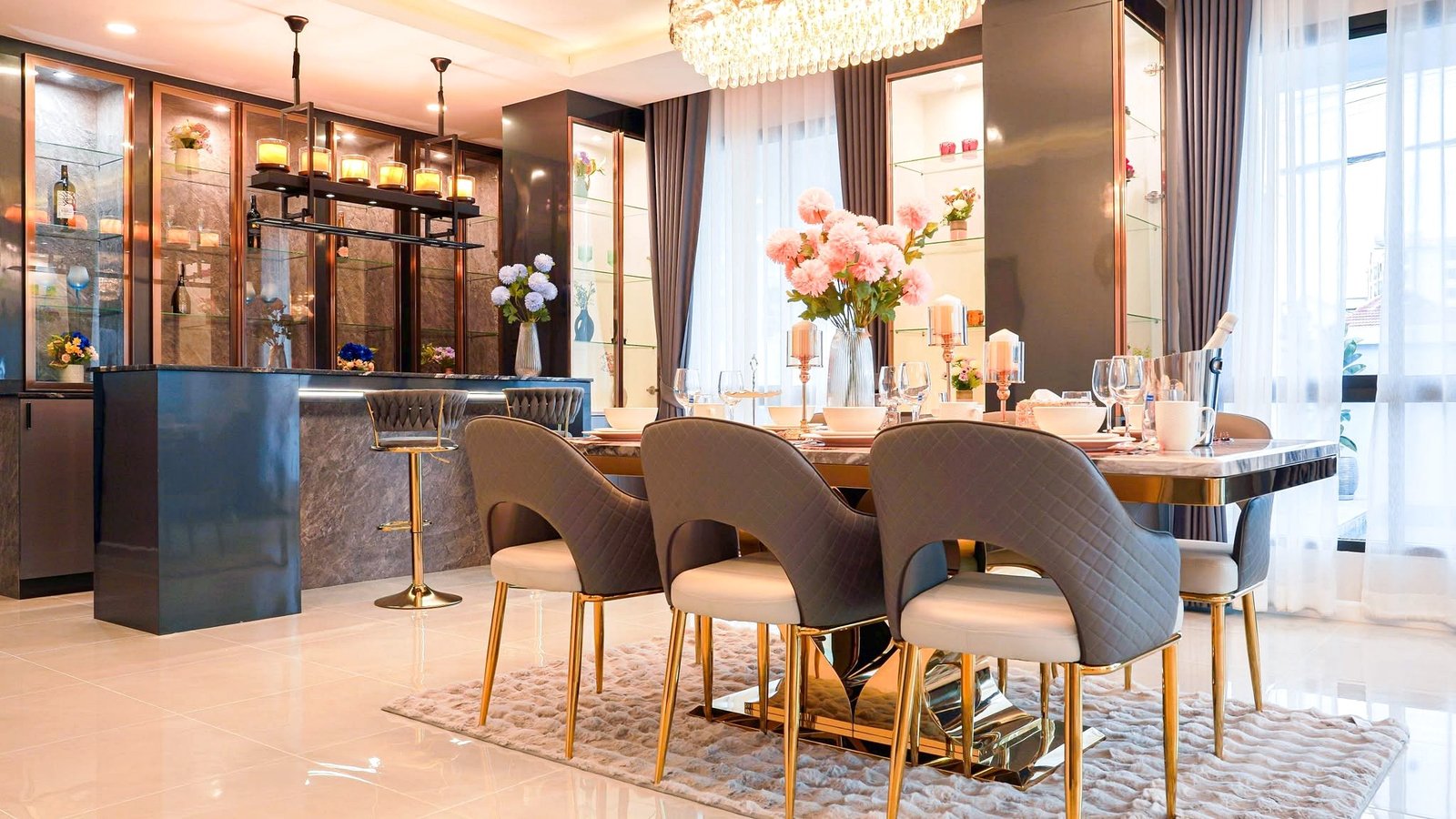 Luxurious dining room with a marble table set for a formal meal, pink flowers centerpiece, chandelier, and glass display cabinets.