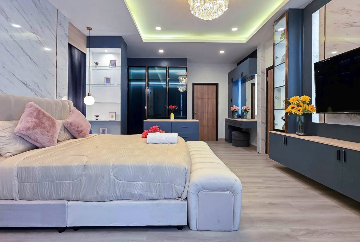 Luxurious modern bedroom with a large upholstered bed, pink cushions, and a flat-screen TV on a marble-adorned wall.