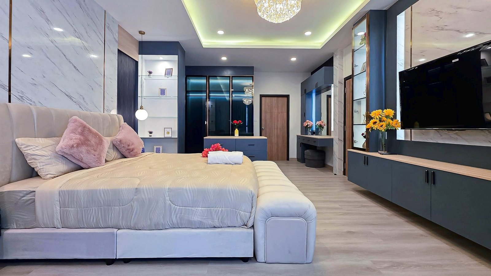 Luxurious modern bedroom with a large upholstered bed, pink cushions, and a flat-screen TV on a marble-adorned wall.