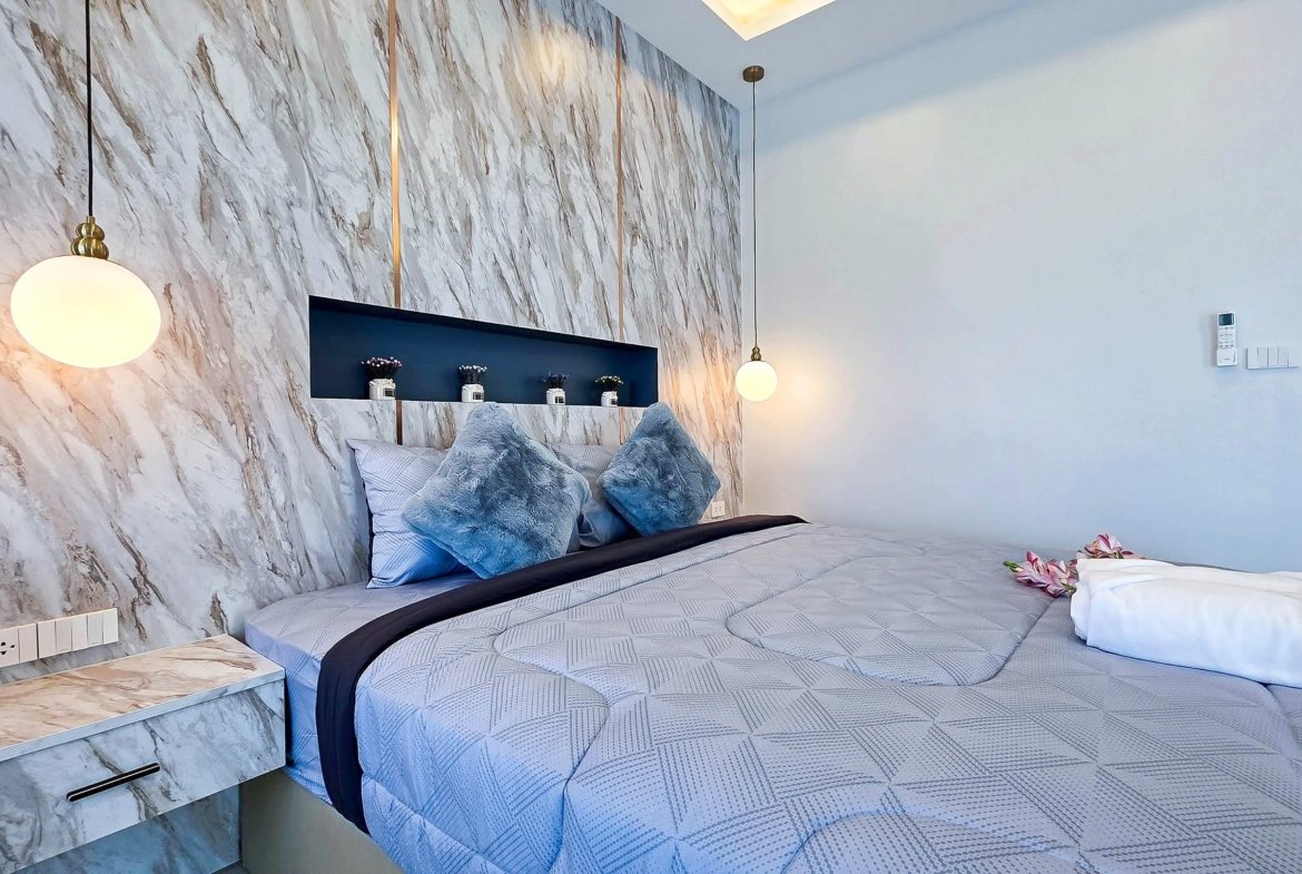 Bedroom with a marble feature wall, round globe pendant lights, and a bed with blue-gray pillows and patterned bedding.