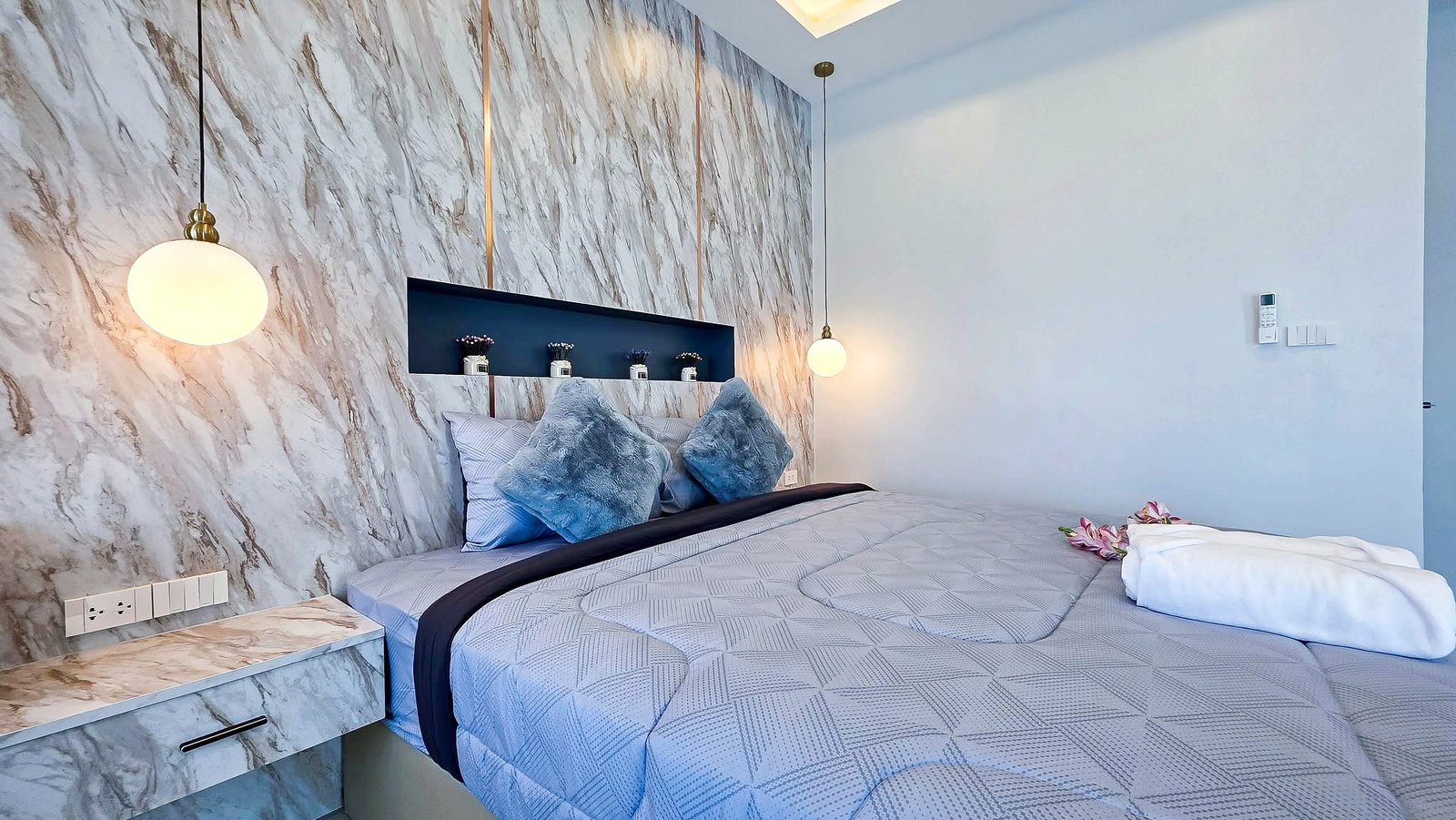 Bedroom with a marble feature wall, round globe pendant lights, and a bed with blue-gray pillows and patterned bedding.