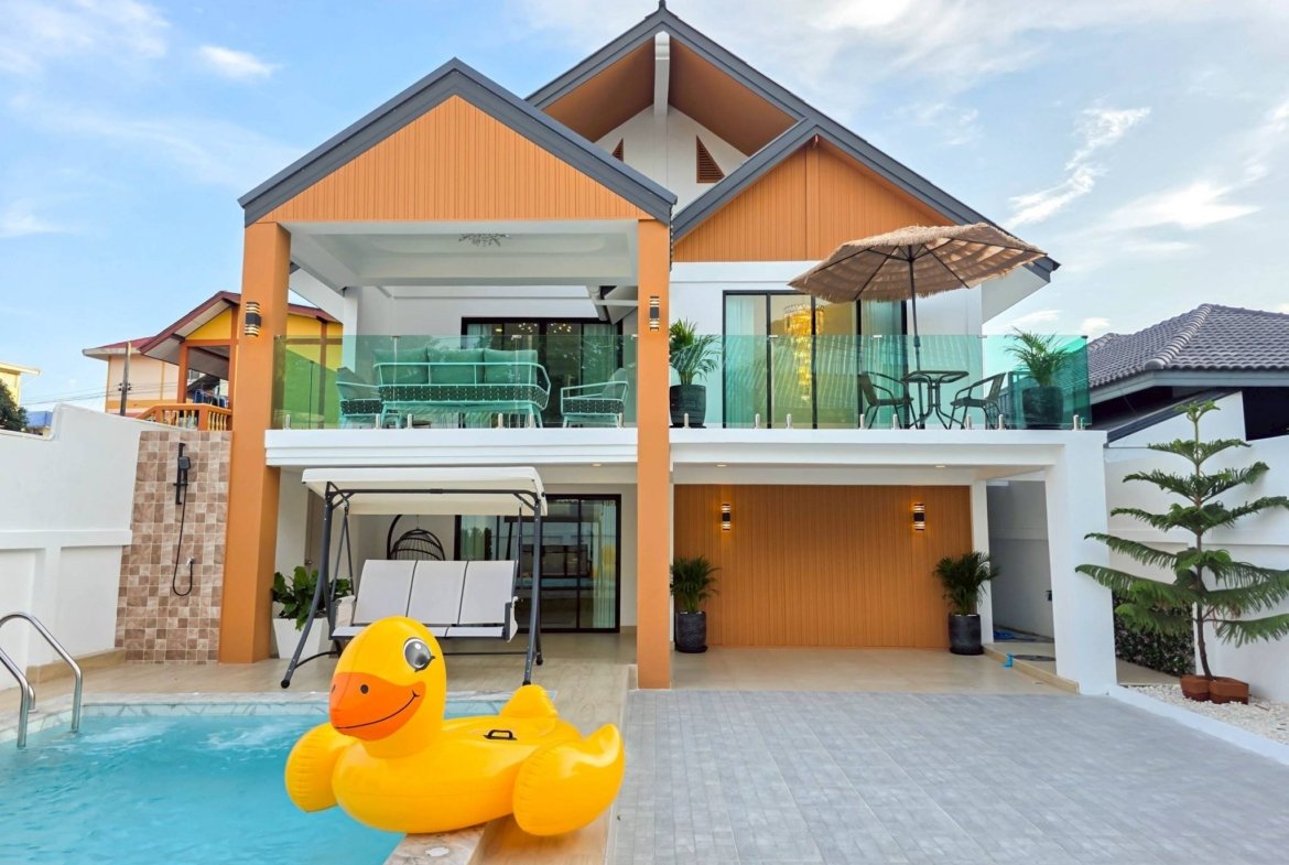 Modern two-story house with orange siding, glass balcony, and a swimming pool with a large yellow inflatable duck in the foreground.