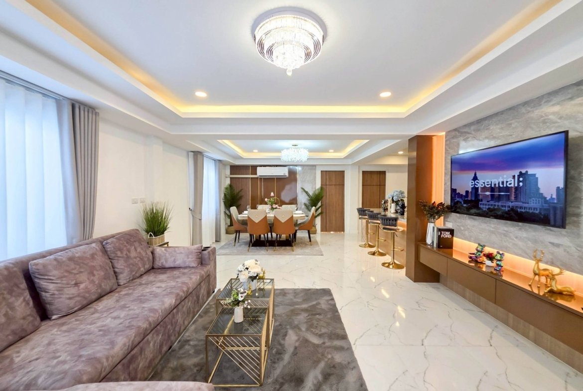Modern open-plan living and dining room with a purple sofa, glass tables, and a crystal chandelier.