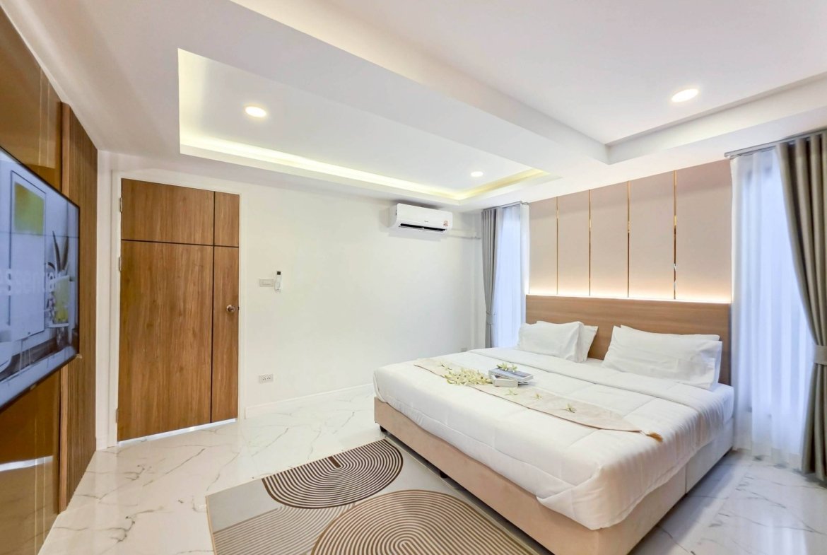 Modern hotel bedroom with a large bed, white linens, and a light wood headboard; marble floor and patterned concentric-circle rug.