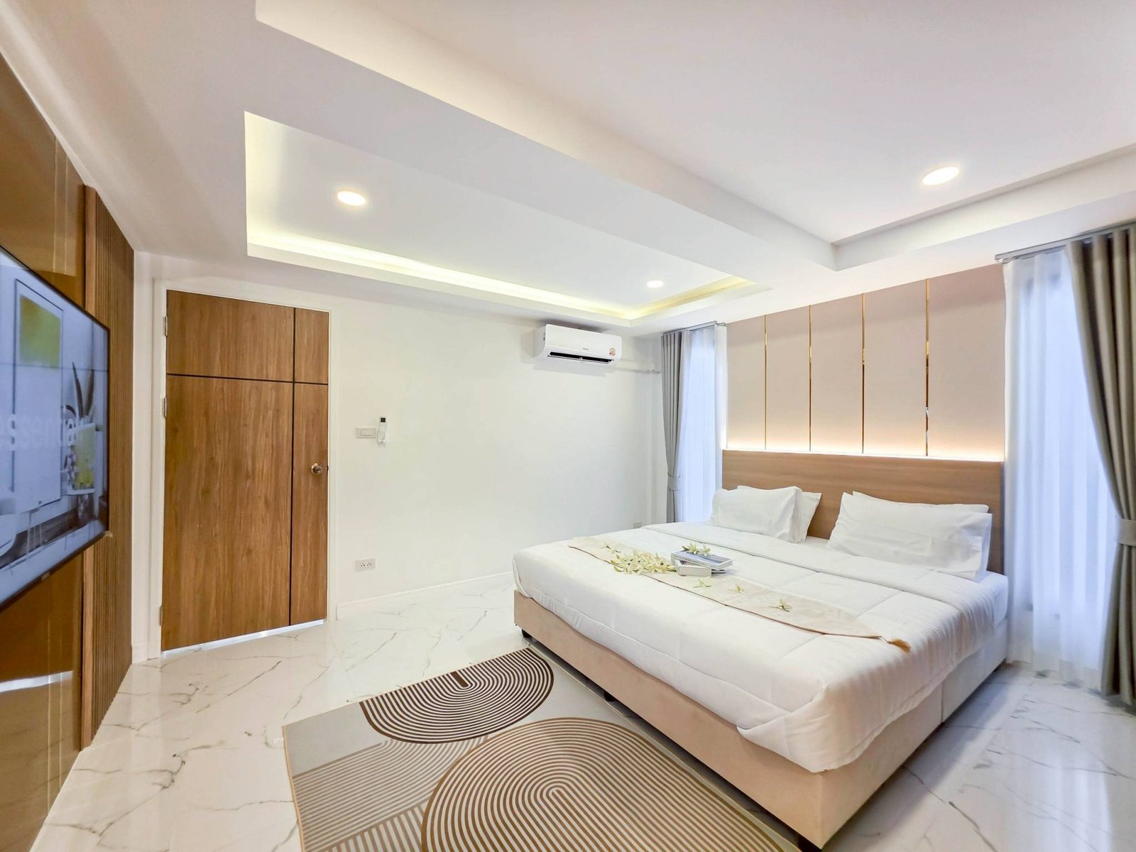 Pool_Villa_South_Pattaya_Sale_Dlh498_13 Modern hotel bedroom with a large bed, white linens, and a light wood headboard; marble floor and patterned concentric-circle rug.