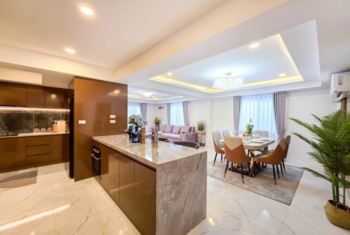 Open-plan kitchen and dining area featuring a marble island, dark brown cabinets, and a crystal chandelier above the dining table.