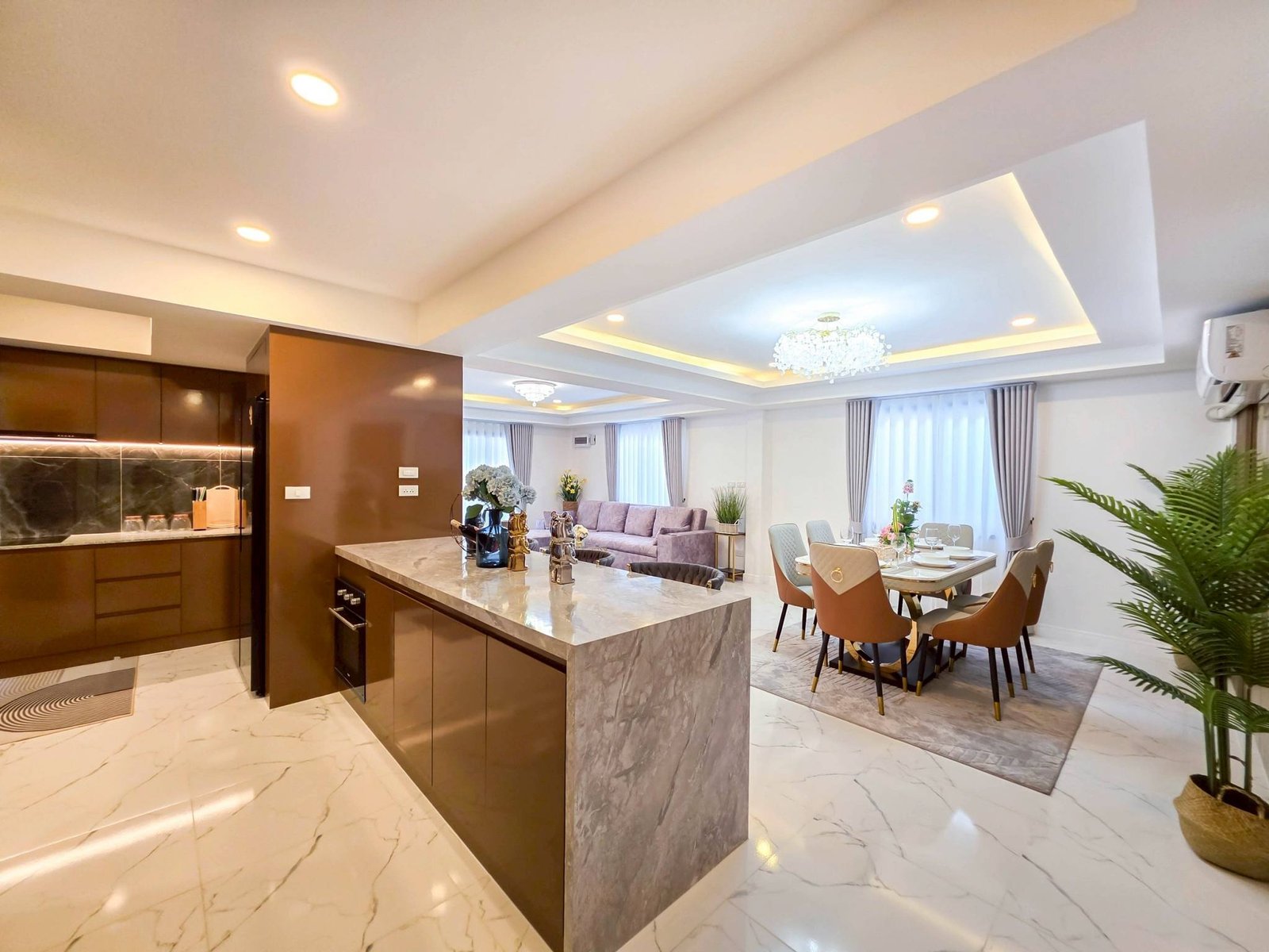 Pool_Villa_South_Pattaya_Sale_Dlh498_15 Open-plan kitchen and dining area featuring a marble island, dark brown cabinets, and a crystal chandelier above the dining table.