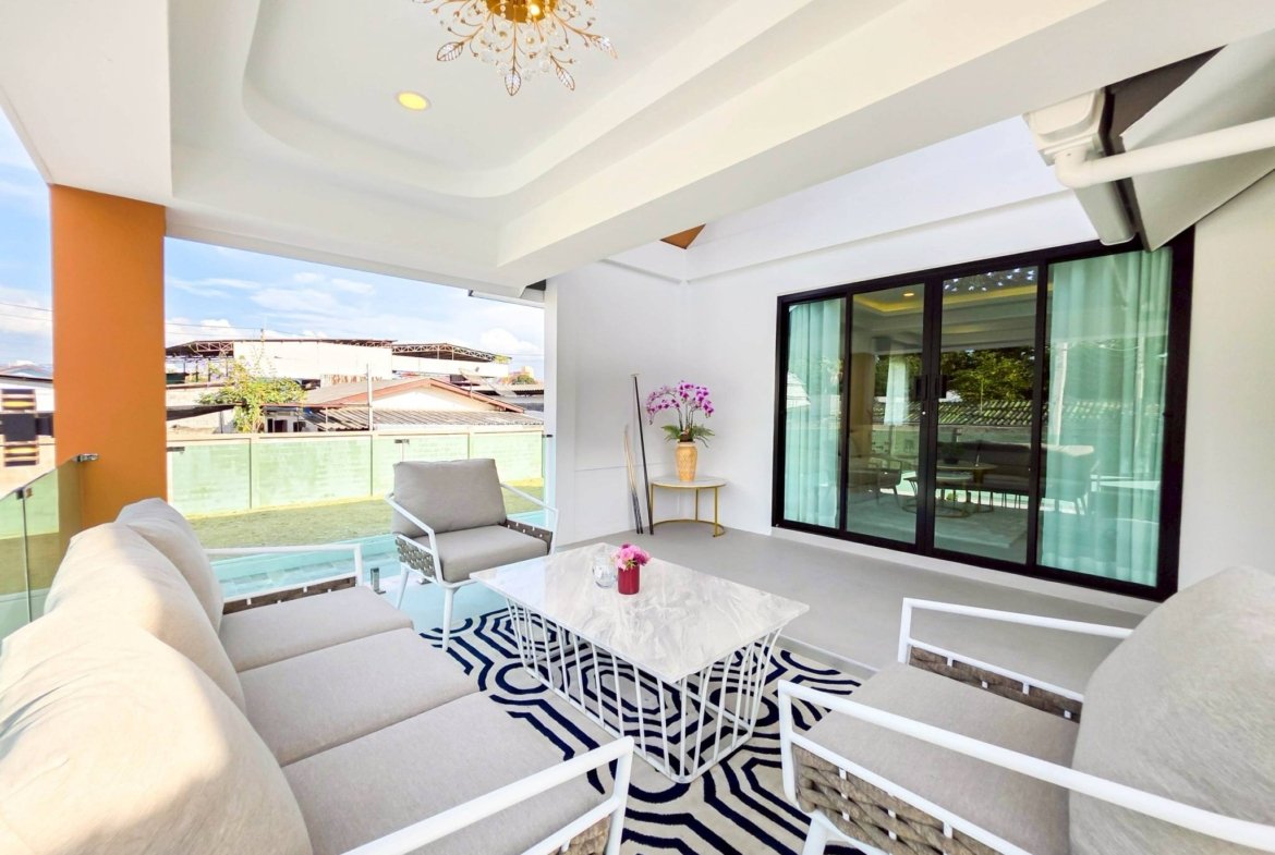 Outdoor balcony seating area with beige sectional sofa, white metal-framed chairs, a white marble table, and a black-and-white zebra rug under a bright ceiling light.