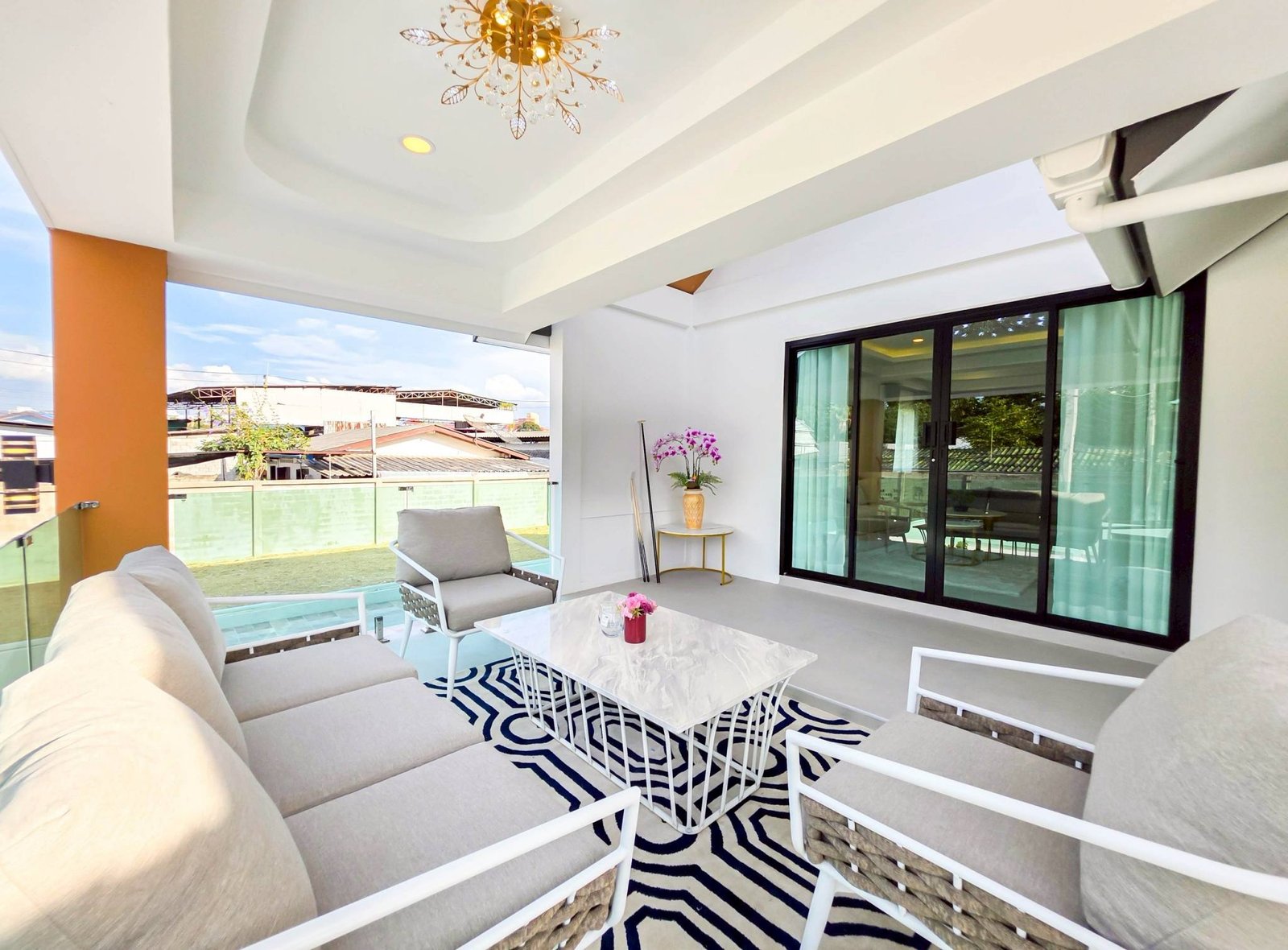 Pool_Villa_South_Pattaya_Sale_Dlh498_19 Outdoor balcony seating area with beige sectional sofa, white metal-framed chairs, a white marble table, and a black-and-white zebra rug under a bright ceiling light.