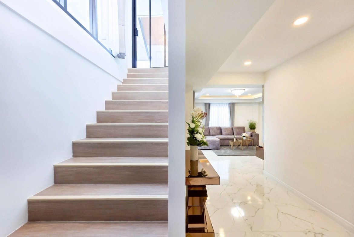 Modern interior split view: wooden staircase on the left and a living area with marble flooring on the right.