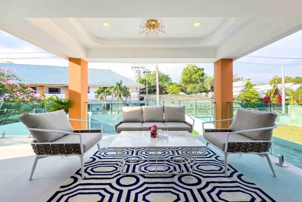 Covered outdoor seating area with cream sofas, white coffee table, and a bold black-and-white geometric rug under a decorative chandelier.
