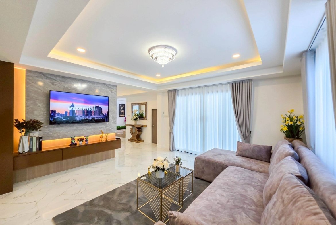 Luxurious living room with marble floors, beige sofa, glass coffee tables, and a crystal chandelier centerpiece.
