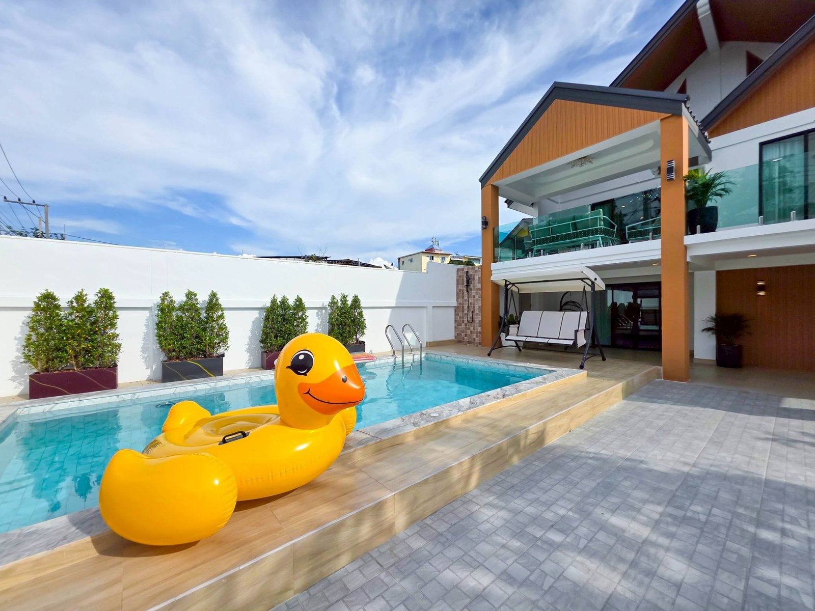 Pool_Villa_South_Pattaya_Sale_Dlh498_33 Residential pool deck with oversized yellow rubber duck floats in the water and modern outdoor furniture under blue sky, contemporary home exterior in the background.