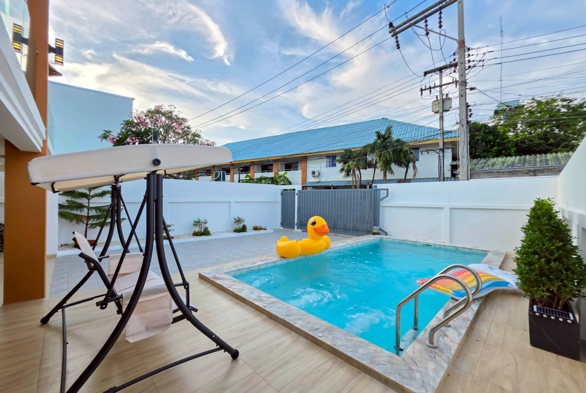 Poolside backyard with a yellow inflatable duck, lounge chairs, and a swing frame over light wood decking.