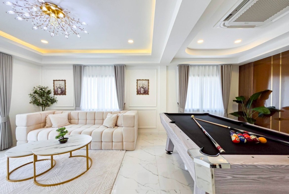 Bright modern living room with a white tufted sectional sofa, glass-top coffee tables, and potted plants under a decorative chandelier.