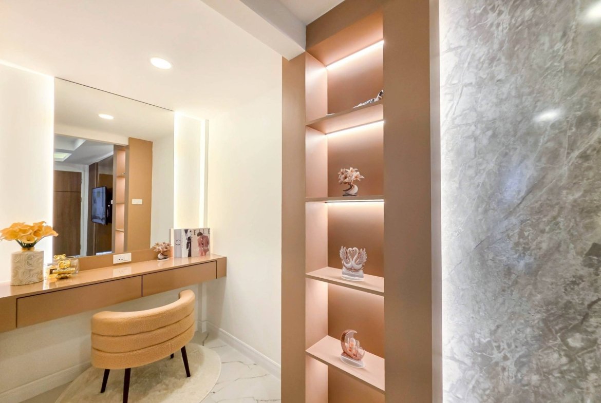Modern vanity with a long beige counter, round stool, and a tall backlit shelf unit displaying small decor against a marble wall on the right.