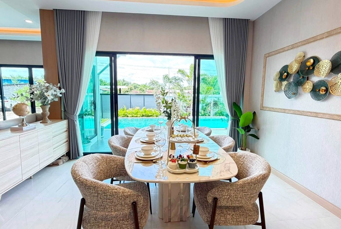 Elegant dining area with a round glass table set for a meal, surrounded by beige patterned chairs and a pool view through glass doors.