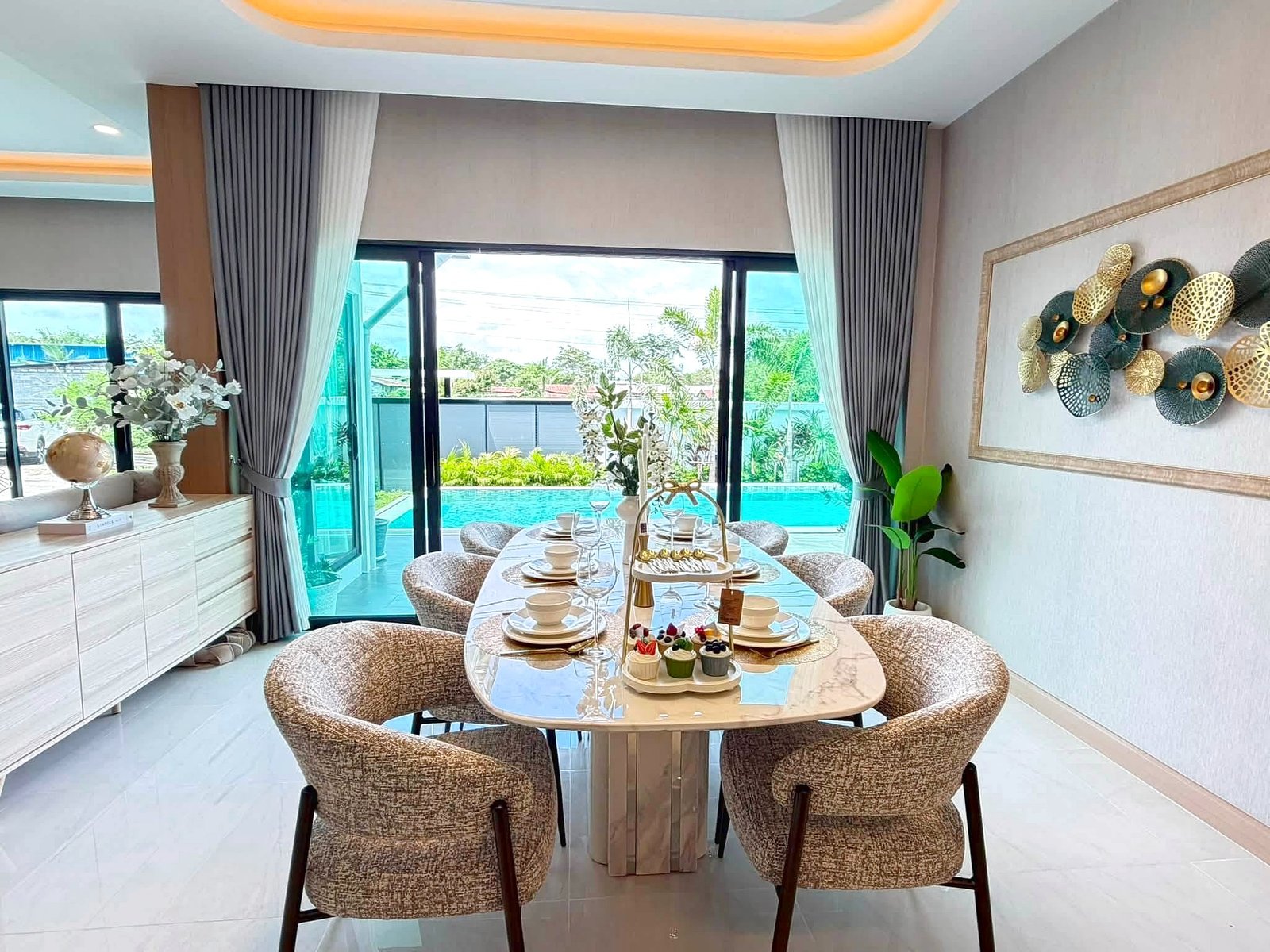 Poolvilla_Khaomakok_Pattaya_Dlh583_12 Elegant dining area with a round glass table set for a meal, surrounded by beige patterned chairs and a pool view through glass doors.