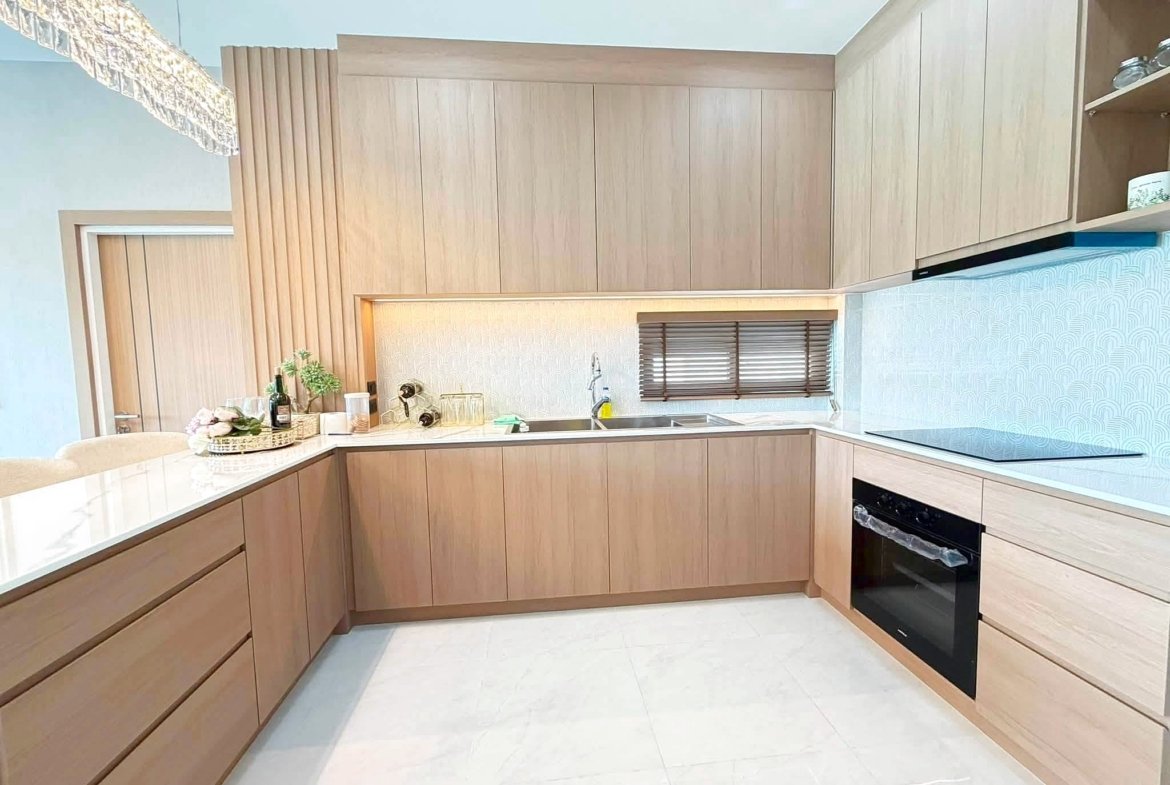 Modern L-shaped kitchen with light wood cabinets, marble countertops, and built-in oven on the right.