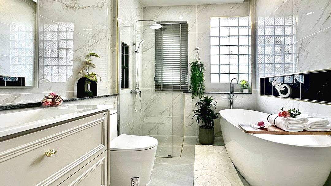 Luxurious bathroom with white marble walls, glass shower, a freestanding tub, and potted plants.
