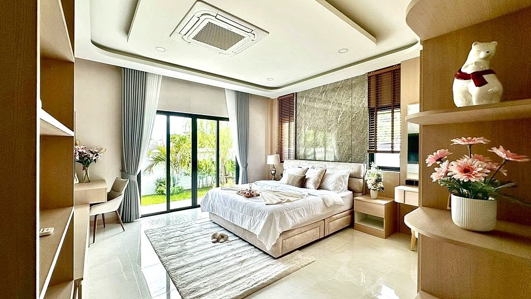 Bright modern hotel bedroom with a king bed, beige furnishings, and glass doors opening to a garden view outside.