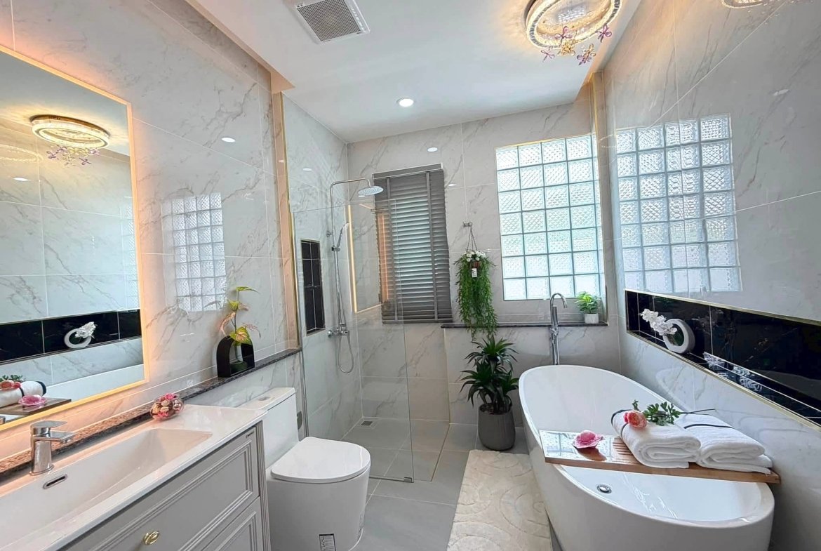 Luxurious marble bathroom with a freestanding oval tub, double vanity, backlit mirror, and potted plants. Glass block windows brighten the space.