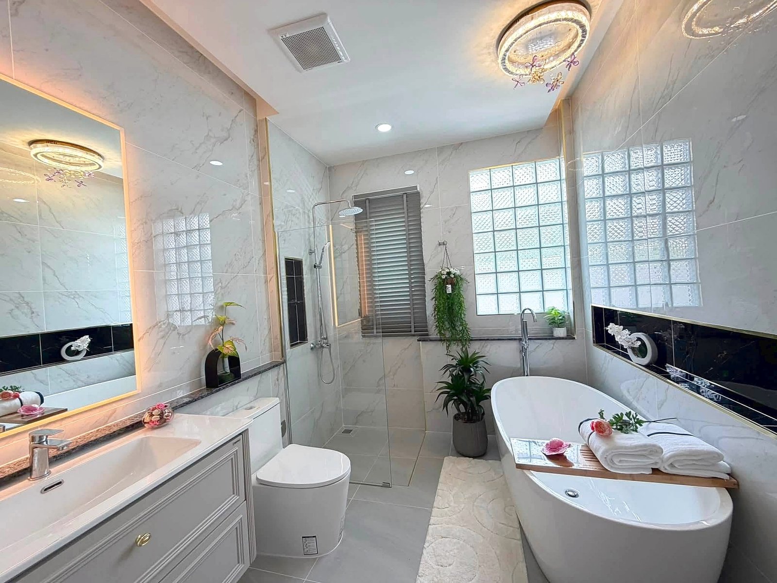 Poolvilla_Khaomakok_Pattaya_Dlh583_8 Luxurious marble bathroom with a freestanding oval tub, double vanity, backlit mirror, and potted plants. Glass block windows brighten the space.