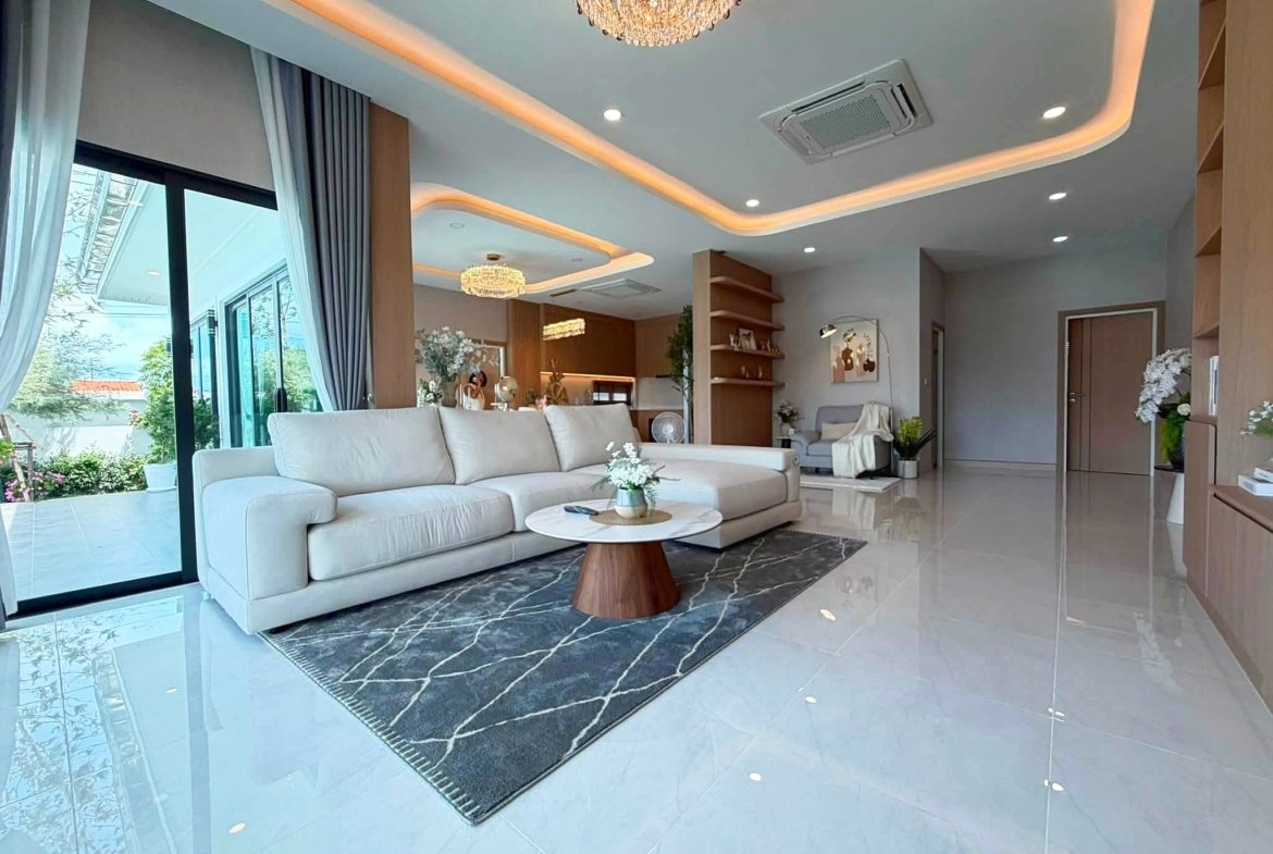 Bright modern living room with white sectional sofa, blue-gray rug, and marble floor tiles, large glass doors, and a crystal chandelier.