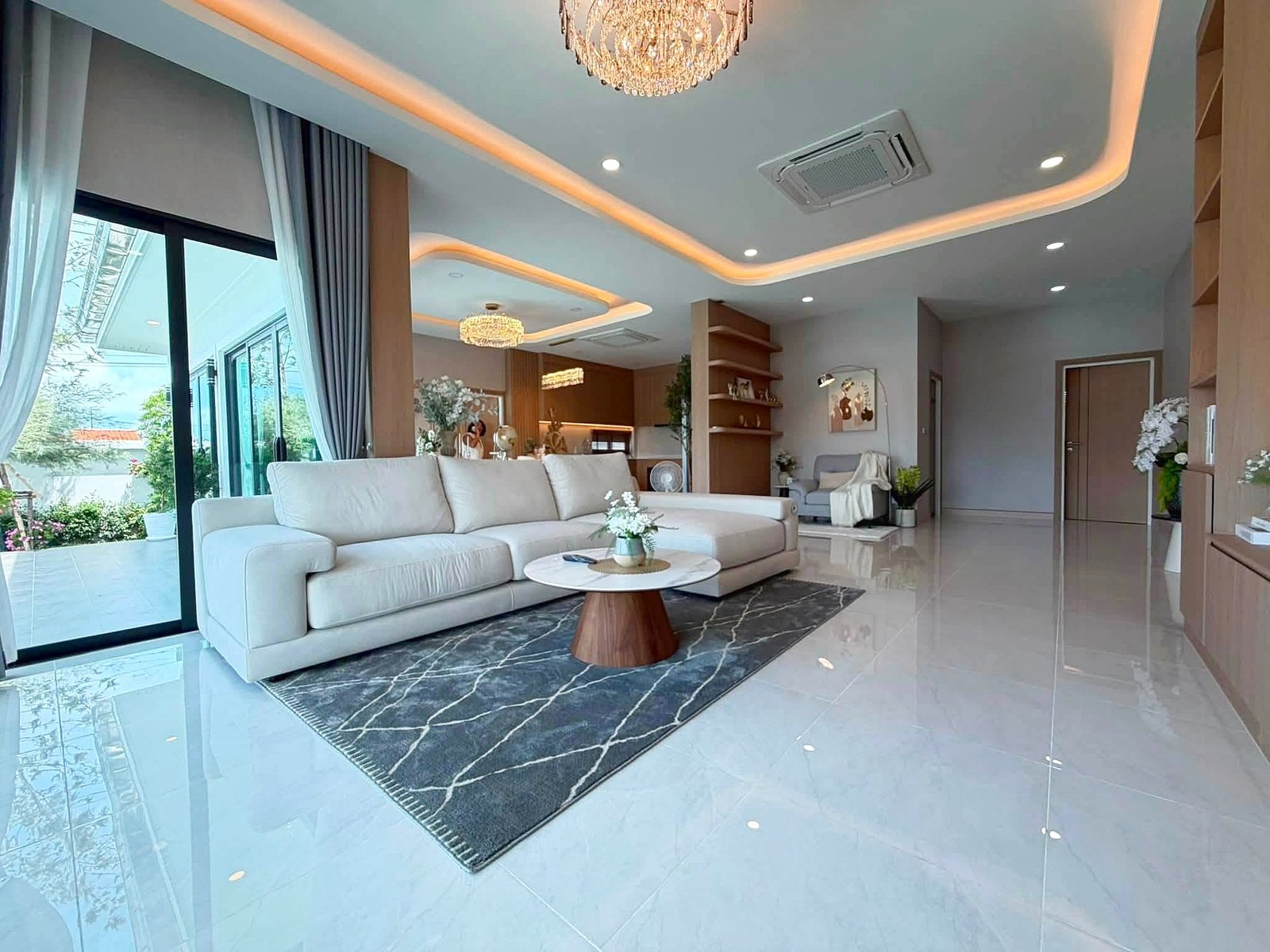 Poolvilla_Khaomakok_Pattaya_Dlh583_9 Bright modern living room with white sectional sofa, blue-gray rug, and marble floor tiles, large glass doors, and a crystal chandelier.