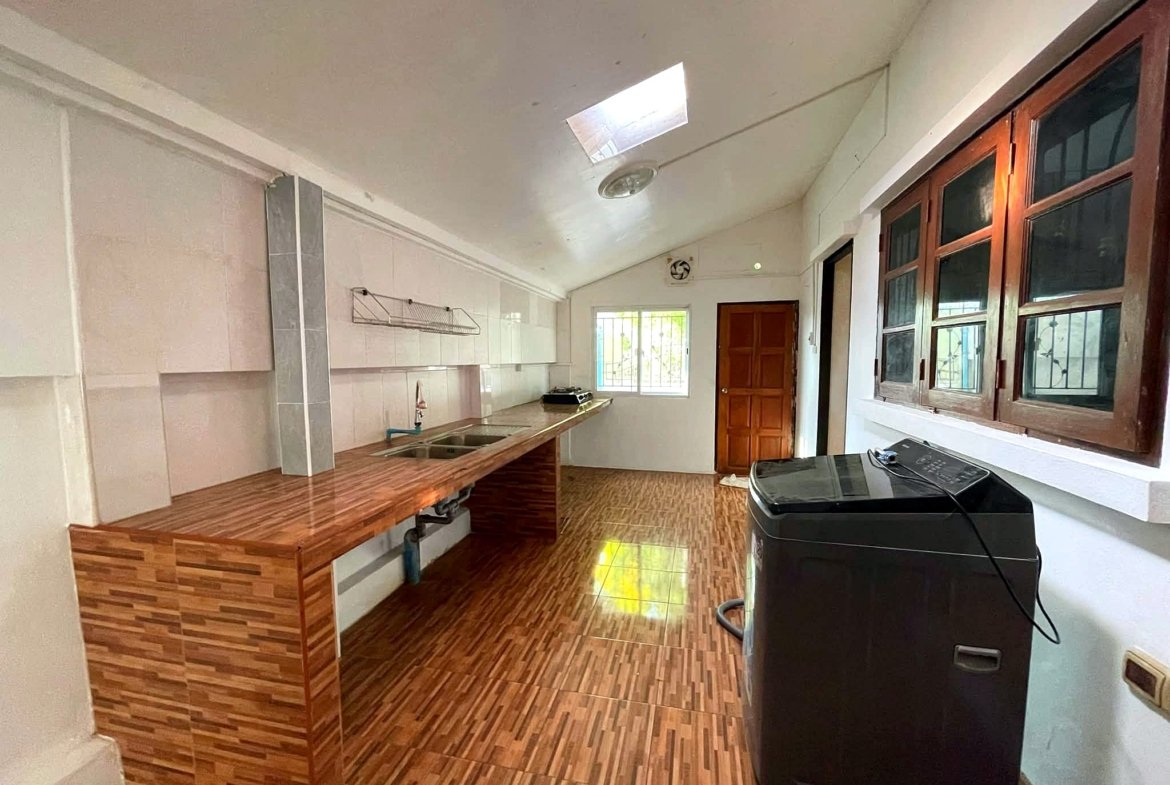 Bright kitchen with a long wooden island and dual sinks, white cabinets, and a skylight; a dark washing machine is in the foreground near the windowed wall on the right.