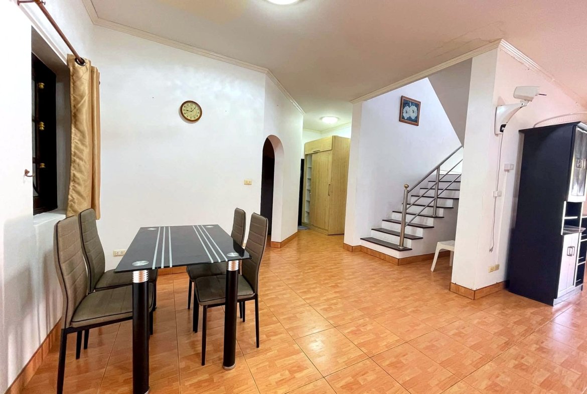 Dining area with a glass tabletop and gray upholstered chairs, tiled floor, and a staircase on the right.
